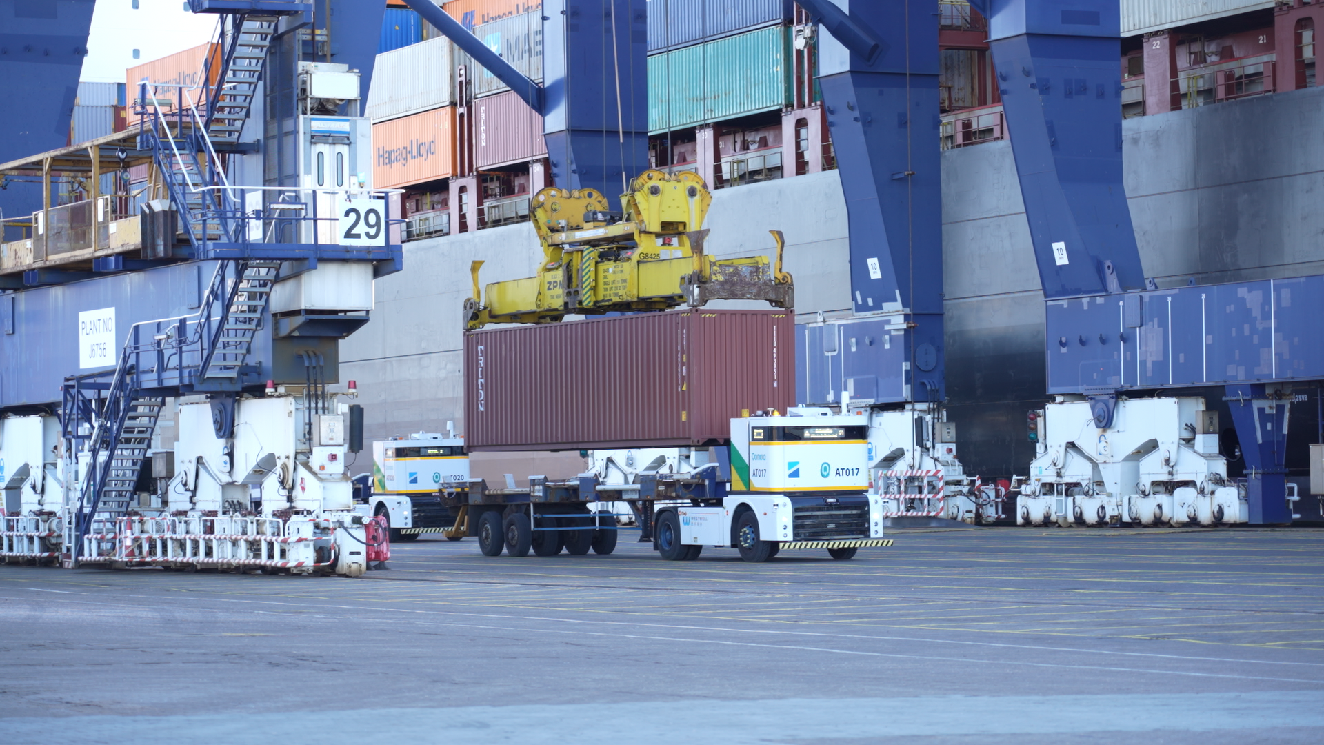 具备 L4 级自动驾驶能力的 Q Truck 全时无人驾驶新能源商用车，在英国菲力斯杜港岸桥下等待集装箱装载，以执行港区内的指定运输任务。